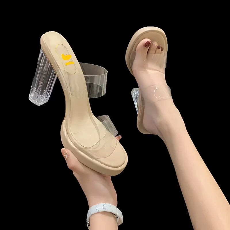 Beige high-heeled shoes with clear heels held by a hand on a black background
